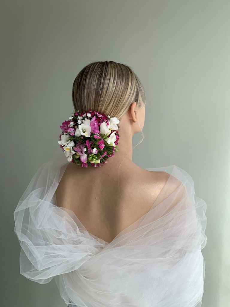 In questa foto, un'acconciatura da sposa con chignon alto decorato con fiori di colore bianco e fucsia