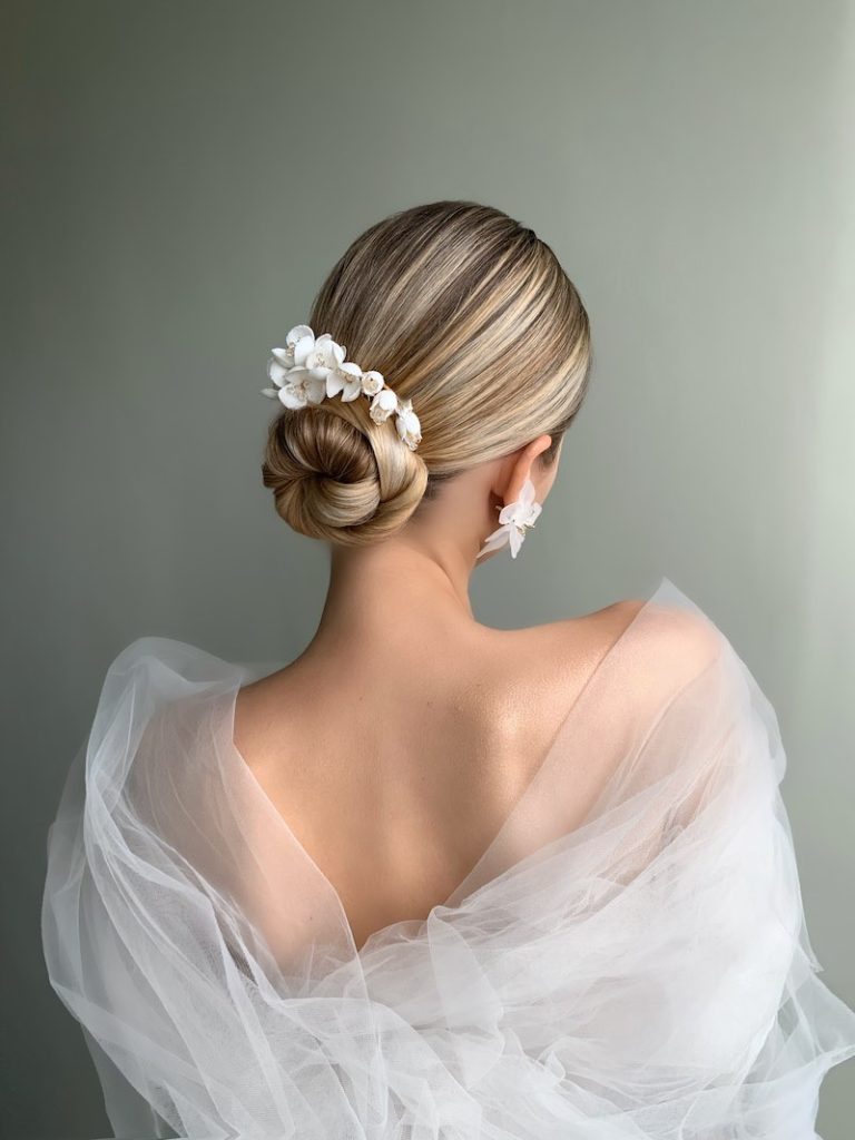 In questa foto, un'acconciatura da sposa con chignon alto decorato con fiori di colore bianco