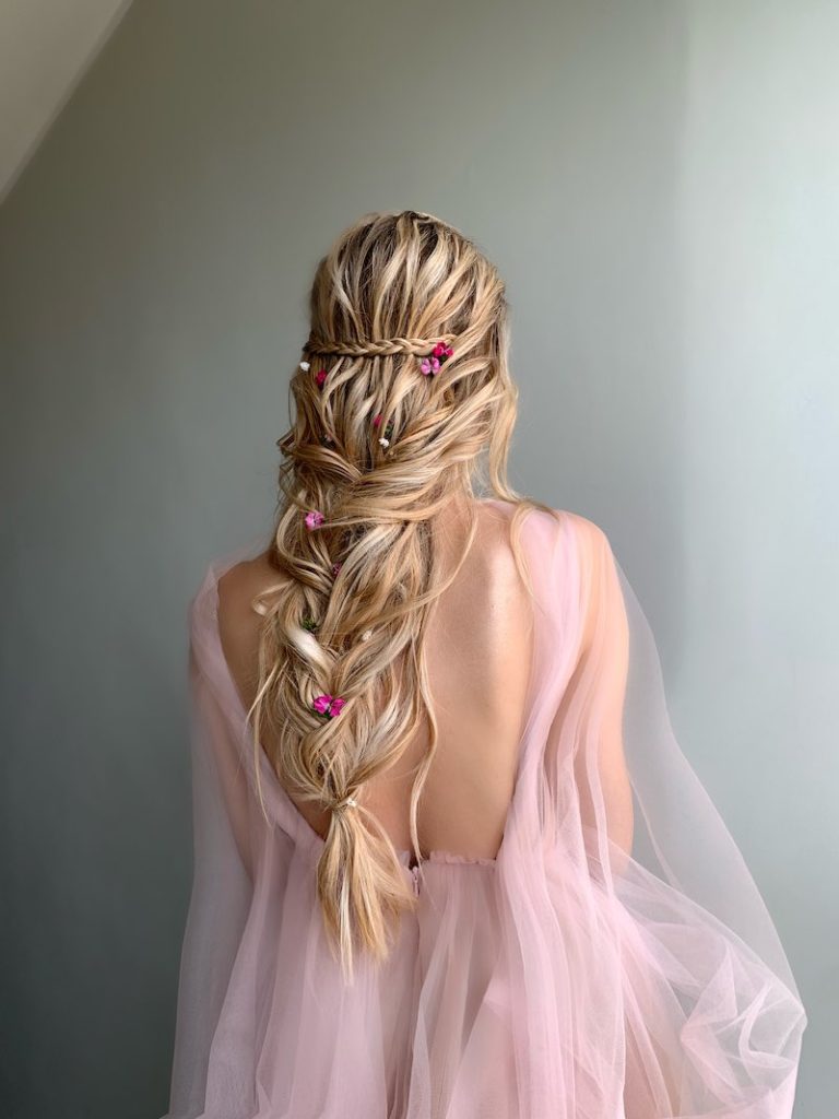 In questa foto, un'acconciatura da sposa semi-raccolta con trecce e fiori di colore fucsia