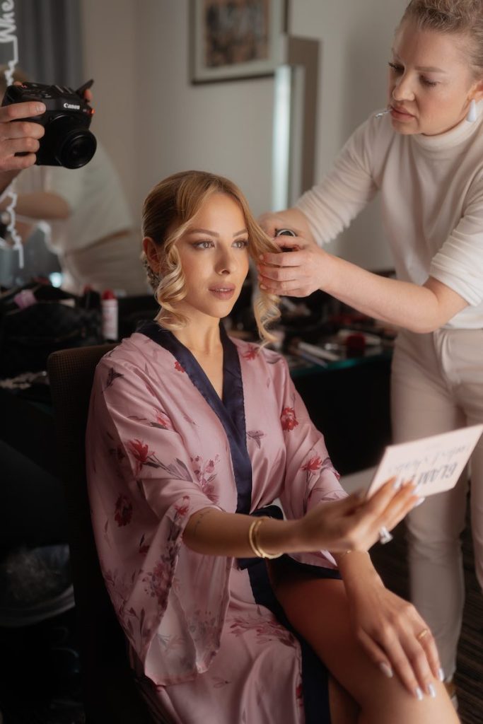 In questa foto, l'hair-stylist Annartstyle sistema l'acconciatura di una spsoa che indossa un kimono di colore rosa e tiene uno specchio nella mano destra