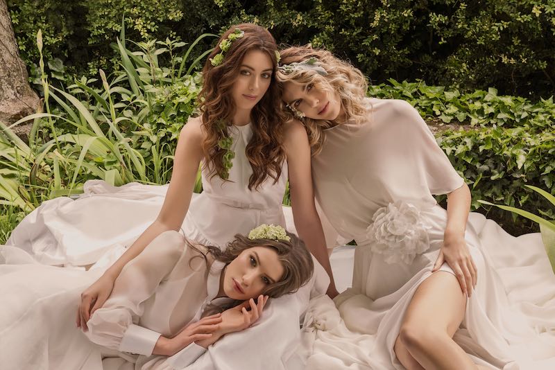 In questa foto, tre modelle posano su un prato con abiti da sposa e beauty look bucolici