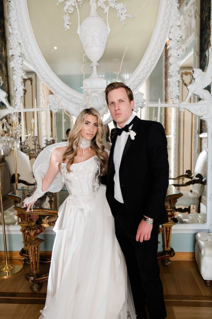 In questa foto, due sposi in un antico palazzo. La sposa indossa un abito principesco con chocker di pizzo. Lo sposo indossa uno smoking