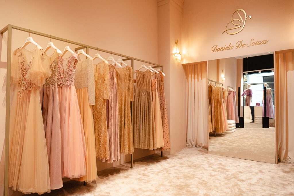Interno dell'atelier Daniela De Souza con vista di alcuni abiti da cerimonia appesi su una rella. GLi abiti sono molto eleganti, con pizzi e tulle tutti nei colori del rosa cipria e altre nuance neutre.