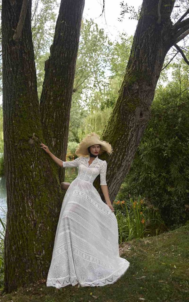 In questa foto, una modella posa con un abito da sposa scivolato in pizzo chantilly, cin maniche a tre quarti, scollo Queen Anne della collezione sposa Elisabetta Polignano 2026