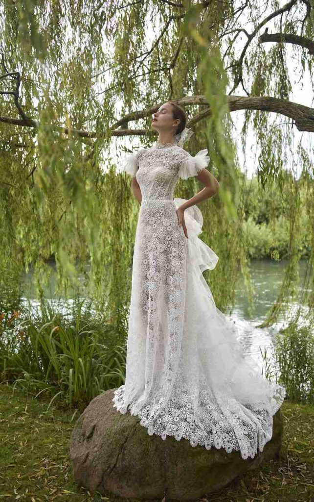 In questa foto, una modella posa con un abito da sposa scivolato in pizzo floreale con strascico a balze 