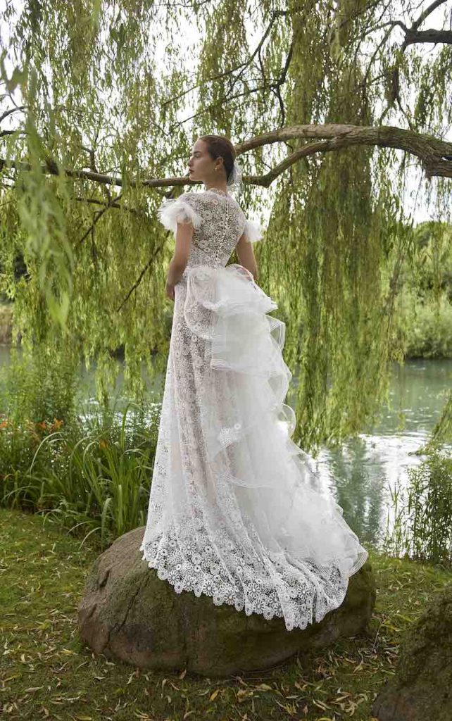 In questa foto, una modella posa con un abito da sposa scivolato in pizzo floreale con strascico a balze 