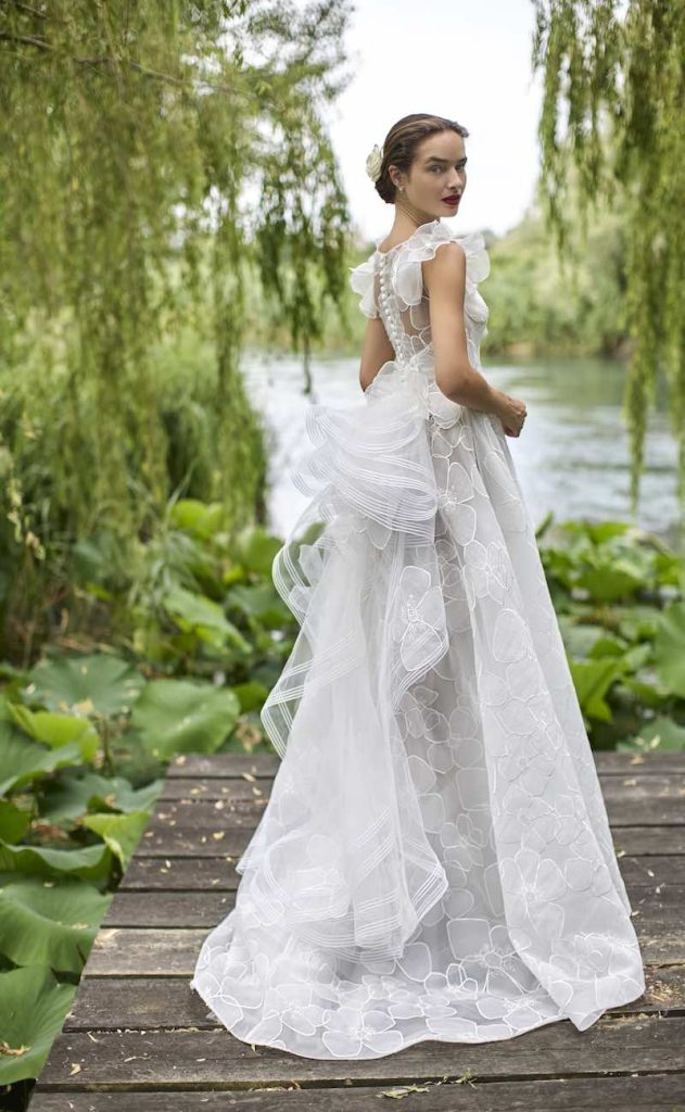 In questa foto, una modella posa con un abito da sposa a A in tulle con disegni floreali e corpetto steccato della collezione sposa Elisabetta Polignano 2026