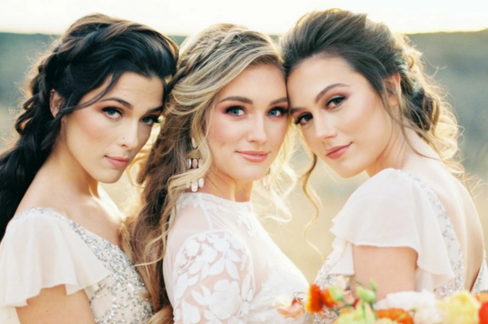 In questa foto, tre donne con capelli raccolti e make-up elegante posano insieme all'aperto, abbracciandosi con dolcezza. I loro volti sono luminosi, con ombretti caldi e sguardi intensi. Questa immagine rappresenta perfettamente l’armonia tra sposa e damigelle, offrendo ispirazione su come scegliere trucco sposa per un look sofisticato e naturale.