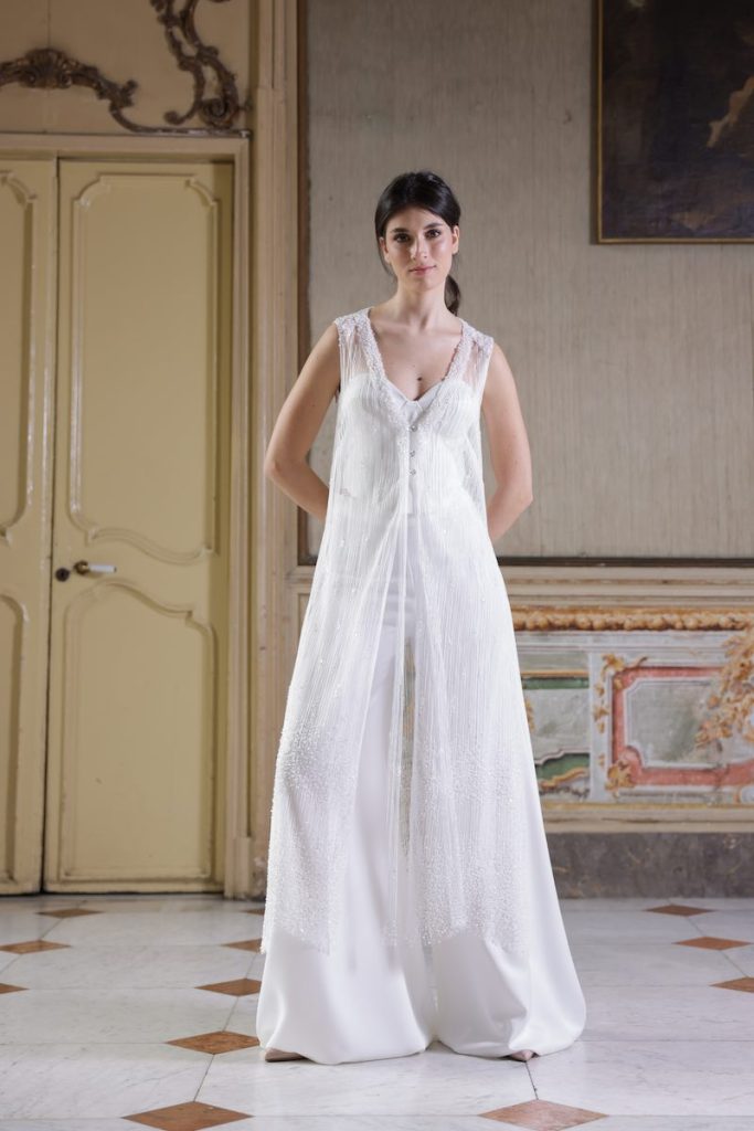 In questa foto, una modella indossa una tuta da sposa Atelier Benedetta  abbinato ad un gilet lungo in tulle ricamato con perline e micropaillettes