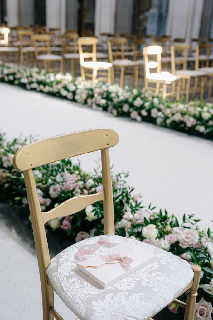 In questa foto, la sedia del matrimonio di Eleonora e Danilo allestita con una Wedding Bag in cartone rigido di colore bianco con nastri di colore rosa. Sullo sfondo il corridoio floreale allestito da Giorgia Pirro