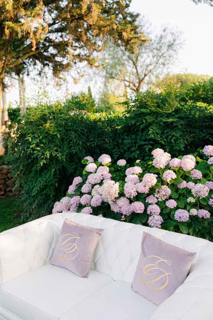 In questa foto, il dettaglio dei cuscini in velluto di colore rosa con il logo degli sposi Eleonora e Danilo, posizionati su un divano di colore bianco posto nella zona lounge del matrimonio