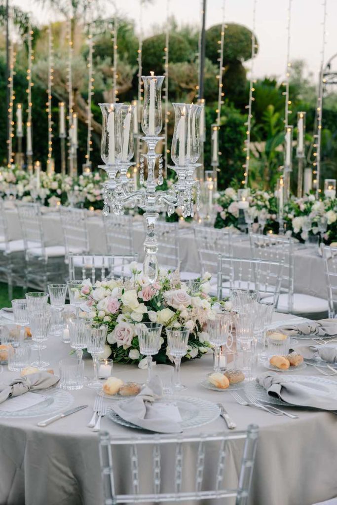 In questa foto, il dettaglio di un tavolo di un ricevimento di nozze nei toni del grigio perla, del rosa e del bianco con tavoli allestiti con fiori, candele e candelabri