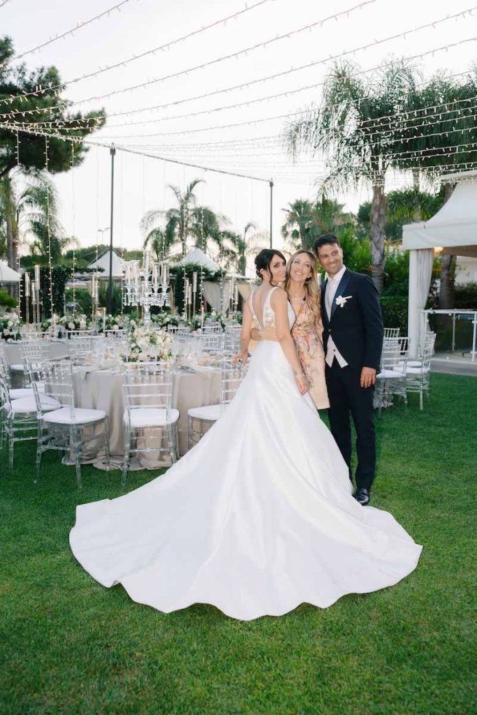 In questa foto, la Wedding Planner Giorgia Pirro abbracciata ai due sposi Eleonora e Danilo davanti all'area del ricevimento allestito su un prato 