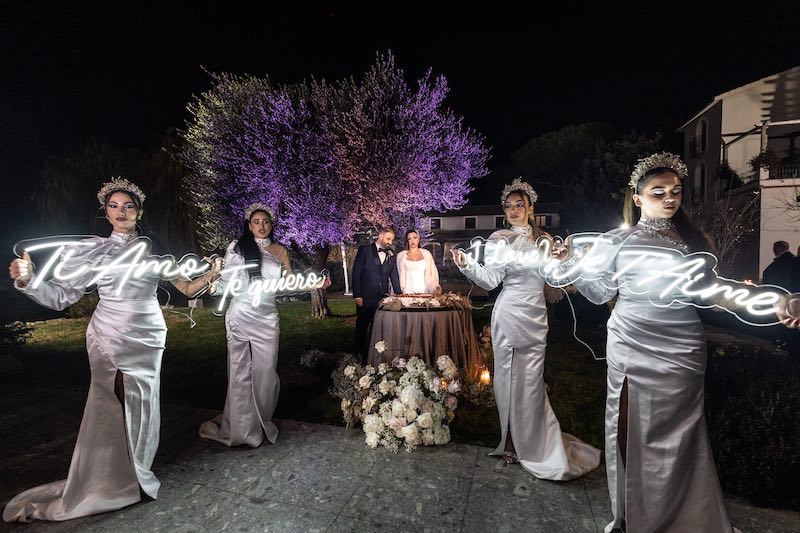 In questa foto, il taglio della torta del matrimonio di Maria Pia e PierPaolo organizzato all'esterno tra performer che tengono in mano scritte luminose con le parole "Ti amo" "Te quiero" " I love you" e Je T'Aime"