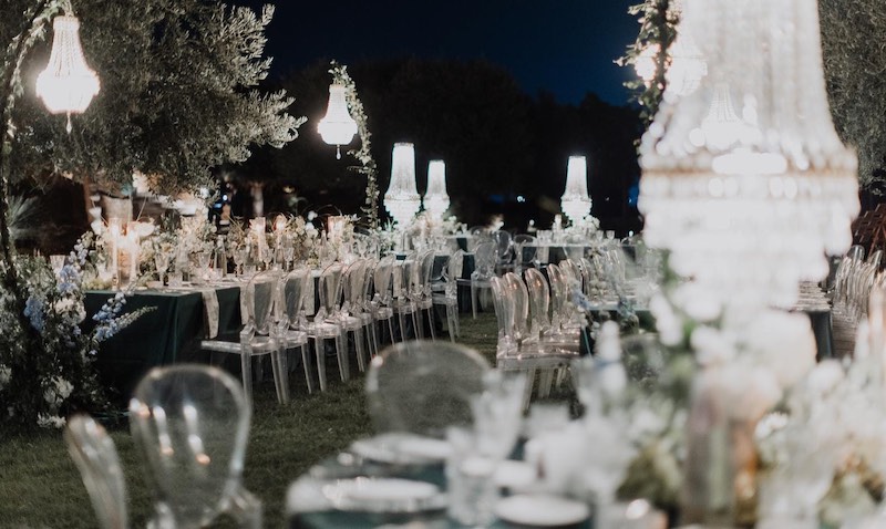 In questa foto, un allestimento di nozze in giardino in stile elegante con candelabri, sedie in plexiglass e tovagliato e fiori nei toni del verde ottanio e bianco firmato Effecreazioni