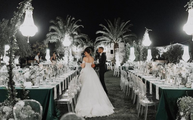 In questa foto, due sposi che guardano il loro allestimento di nozze in giardino in stile elegante con candelabri, sedie in plexiglass e tovagliato e fiori nei toni del verde ottanio e bianco firmato Effecreazioni