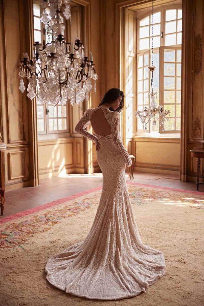 In questa foto, una modella posa di spalle indossando un abito da sposa Oliver Martino 2026 modello a sirena   ricamato con microperle, con scollatura posteriore ad oblò e maniche lunghe