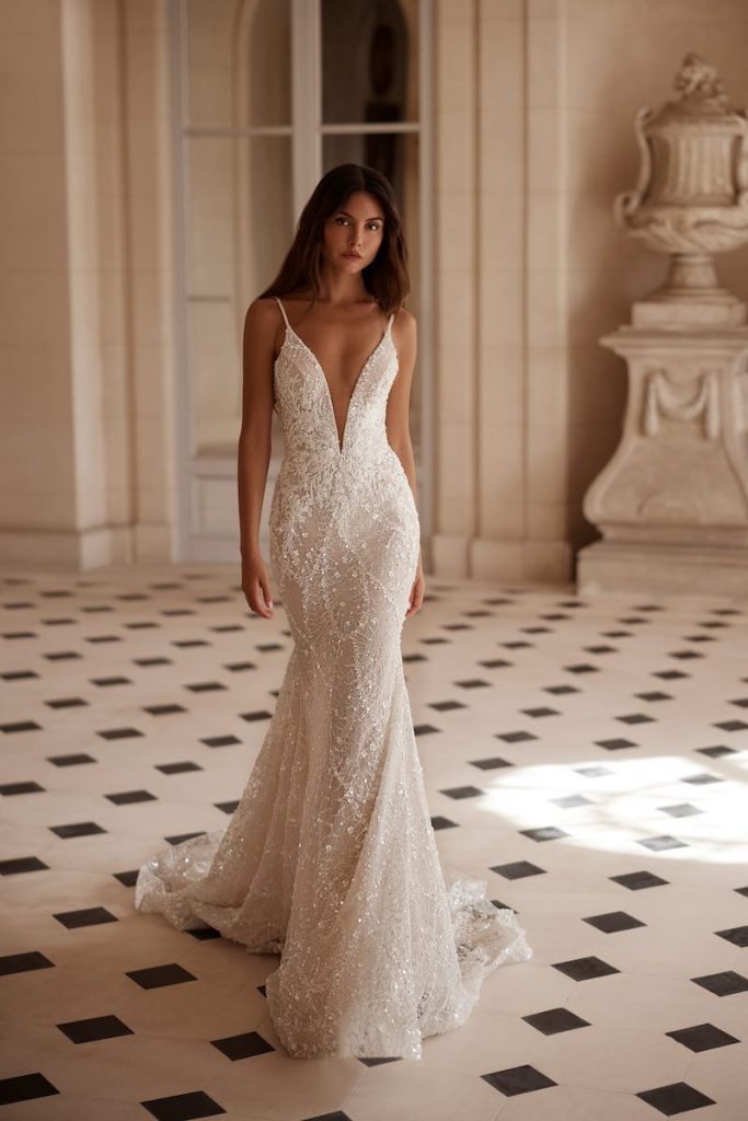 In questa foto, una modella posa di spalle indossando un abito da sposa Yedyna 2026 modello a sirena con scollo a V profondo, microspalline e ricami di perline e paillettes 