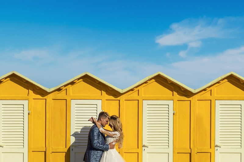 In questa foto, due sposi si abbracciano tenendo la testa abbassata davanti ad una serie di cabine di colore giallo