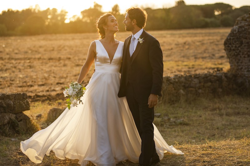 In questa foto, due sposi si guardano sorridenti al tramonto in un campo