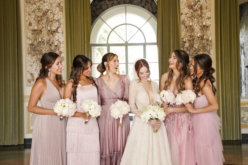 In questa foto di Valeria Santoni, una sposa ride circondata dalle sue damigelle vestite con abiti di varie tonalità di rosa