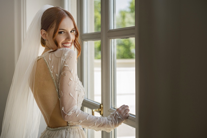 in questa foto di Valeria Santoni, una sposa è girata di tre quarti davanti ad una finestra e sorride guardando la fotografa