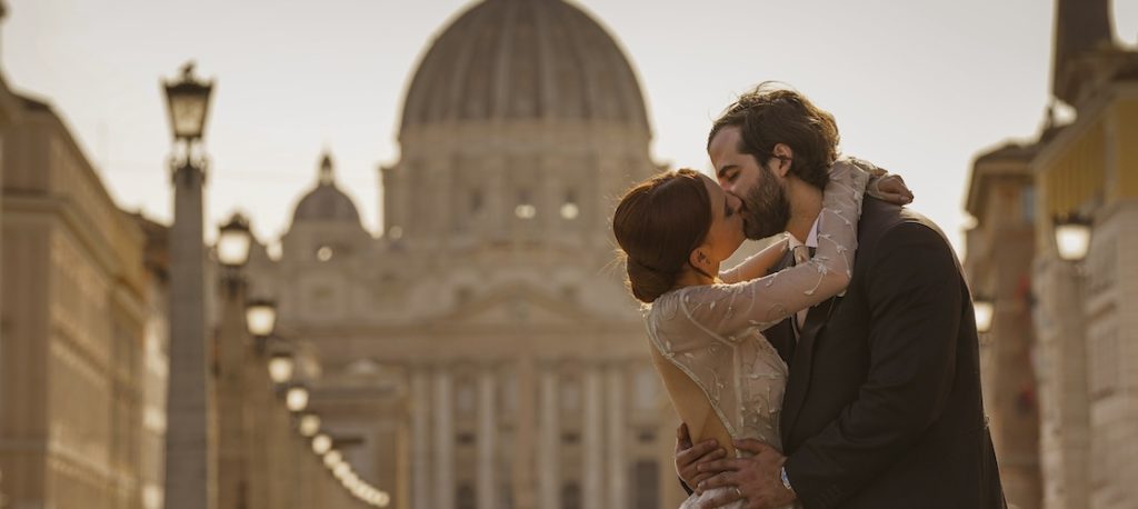 In questa foto di Valeria Santoni due sposi si baciano abbracciati. Sullo sfondo si intravede la cupola di San Pietro