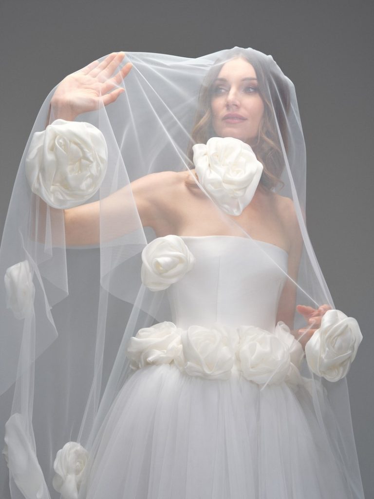 In questa foto, una modella posa indossando un velo da sposa in tulle con applicazioni di maxi rose in mikado di seta
