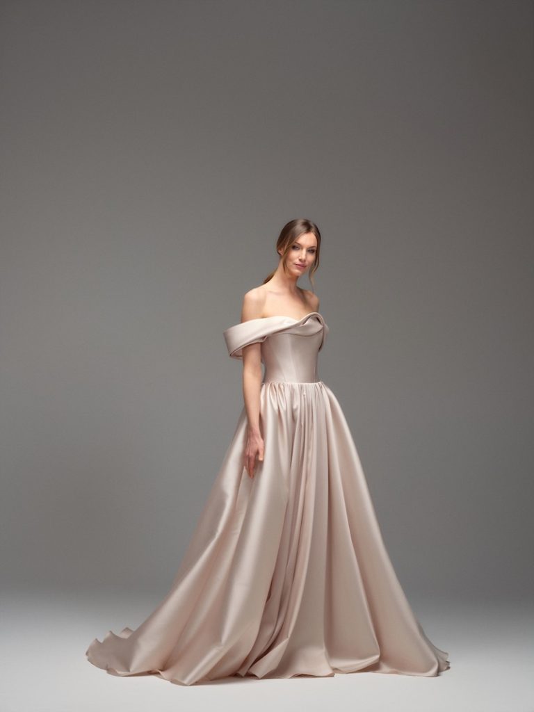 In questa foto, una modella indossa uno degli abiti da sposa Maria Pia Creazioni 2026 di colore rosa cipria, modello ad A con scollo omerale