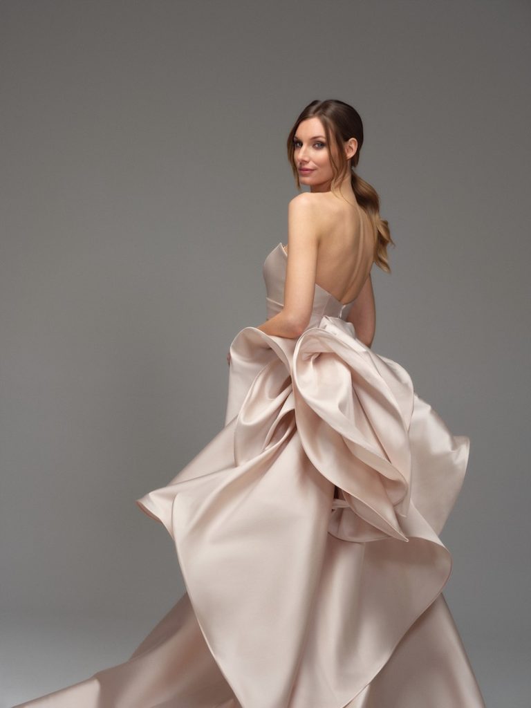 In questa foto, una modella posa di spalle indossando uno degli abiti da sposa Maria Pia Creazioni 2026 di colore rosa cipria con maxi ruches sul retro