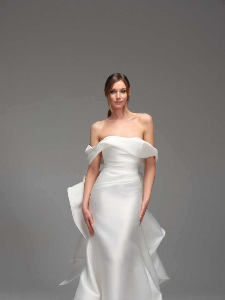 In questa foto, una modella indossa uno degli abiti da sposa Maria Pia Creazioni 2026 a sirena, in mikado di seta, con scollo omerale e strascico con rouches