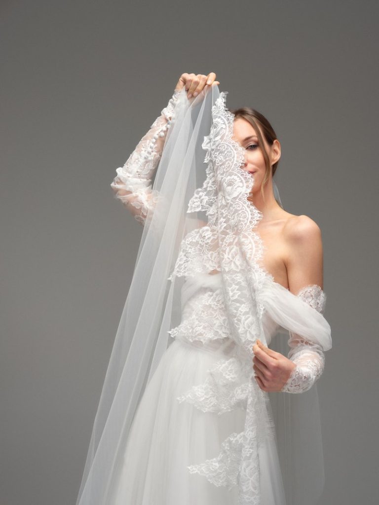 In questa foto, una modella posa mostrando un velo da sposa in tulle con bordatura in pizzo Chantilly
