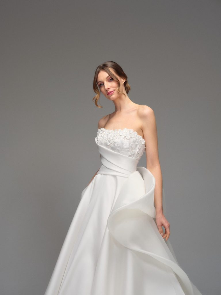 In questa foto, una modella indossa uno degli abiti da sposa Maria Pia Creazioni 2026 modello ampio in mikado di seta e organza, scollatura dritta e applicazioni floreali sul corpetto