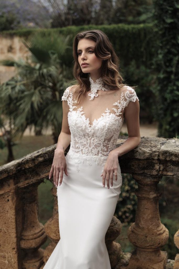 In questa foto, una modella posa appoggiata su una balconata di un palazzo nobiliare indossando un abito a sirena Luisa Sposa 2026 in crêpe e corpetto in pizzo effetto illusion