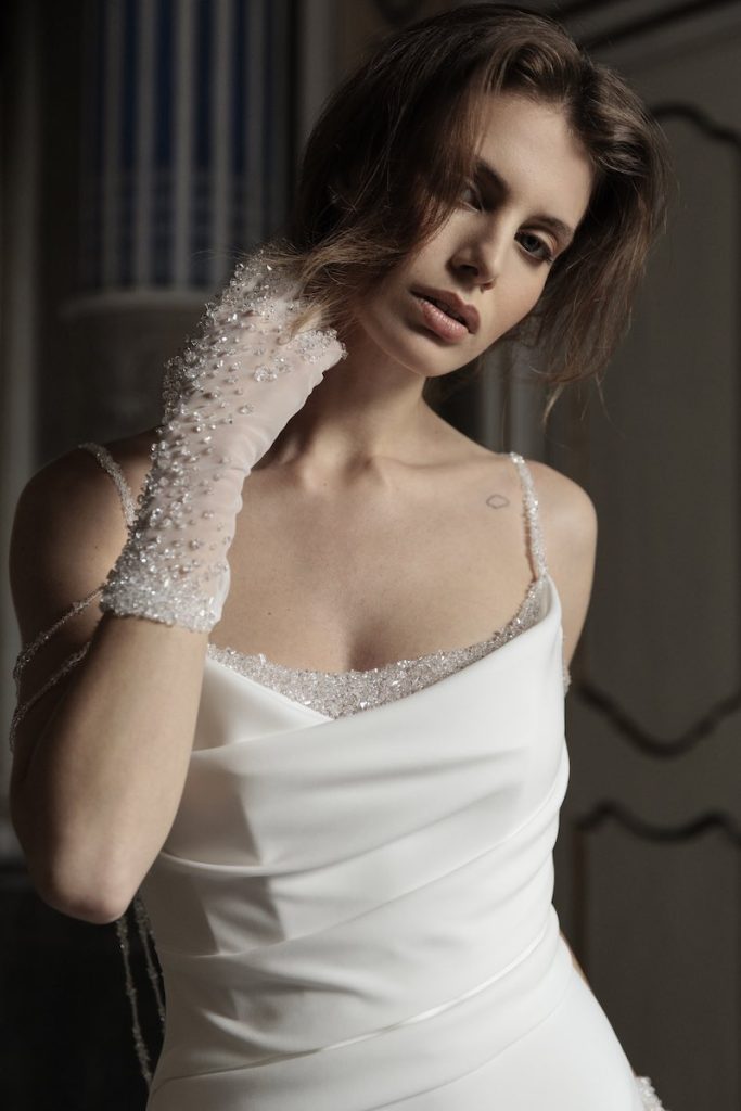 In questa foto, una modella posa indossando un guanto corto da sposa ricamato con perline e cristalli