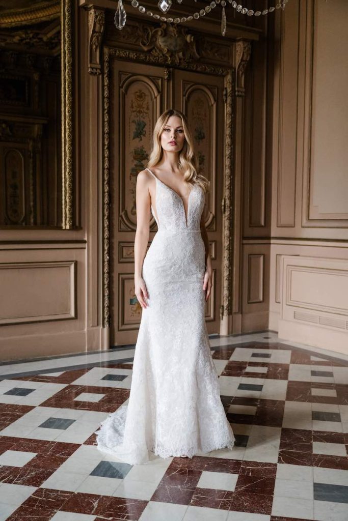 In questa foto, una modella posa nel salone di una dimora storica indossando un abito della collezione sposa Abella 2026 dal taglio a sirena, interamente in pizza e con scollo a V profondo