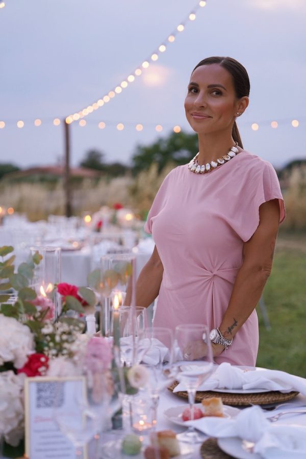 In questa foto, la Wedding Planner Manuela Marrale con un abito di colore rosa confetto e la mani poggiato su un tavolo di nozze decorato da lei