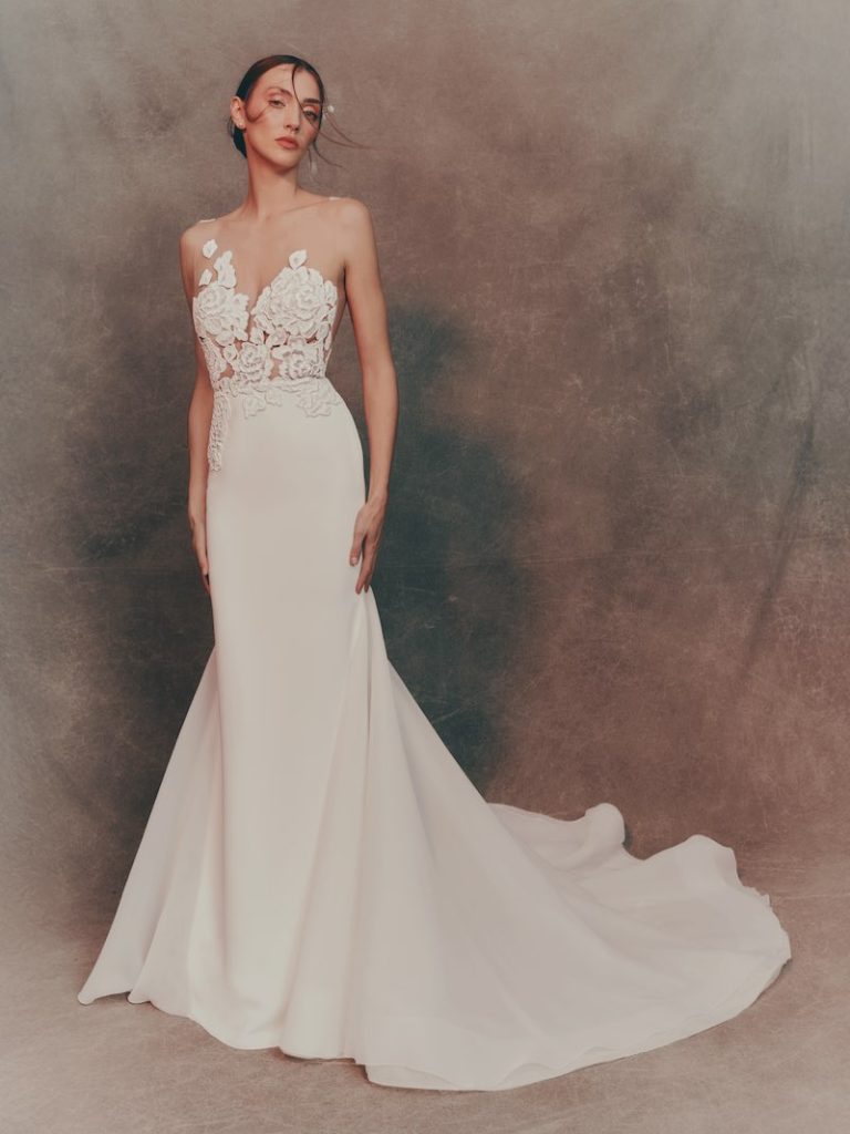 In questa foto una modella posa indossando un abito da sposa a semi sirena in cady con ricami floreali sul corpetto