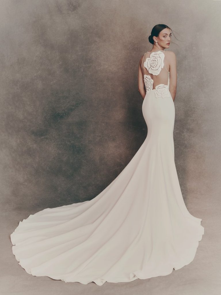 In questa foto una modella posa di spalle indossando un abito da sposa a semi sirena in cady con ricami floreali sulla schiena
