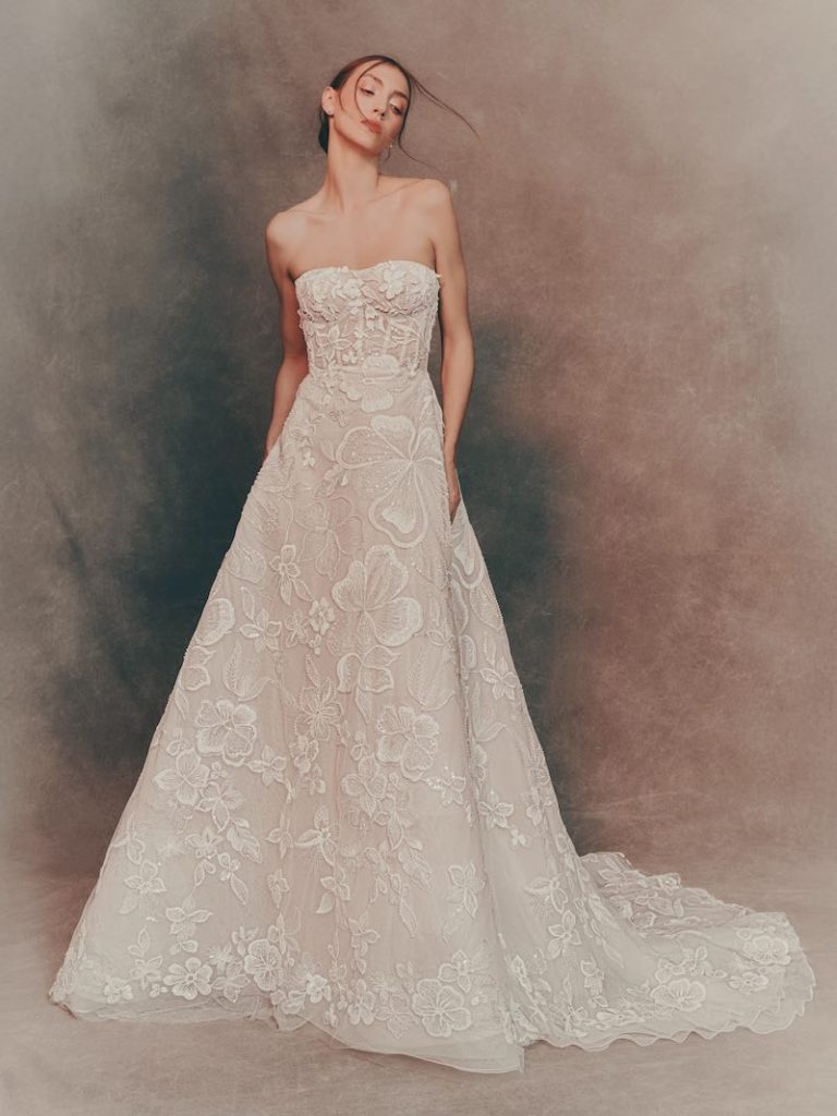 In questa foto, una modella indossa un abito da sposa trasformabile Atelier Pronovias 2026 ad A con bustier steccato con ricami floreali sulla gonna
