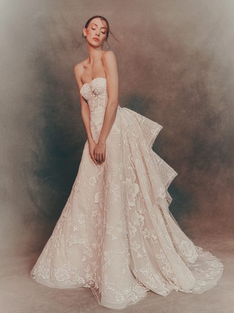 In questa foto una modella indossa un abito da sposa Atelier Pronovias 2026 con scollo a cuore, ricami floreali e drappeggio sul retro