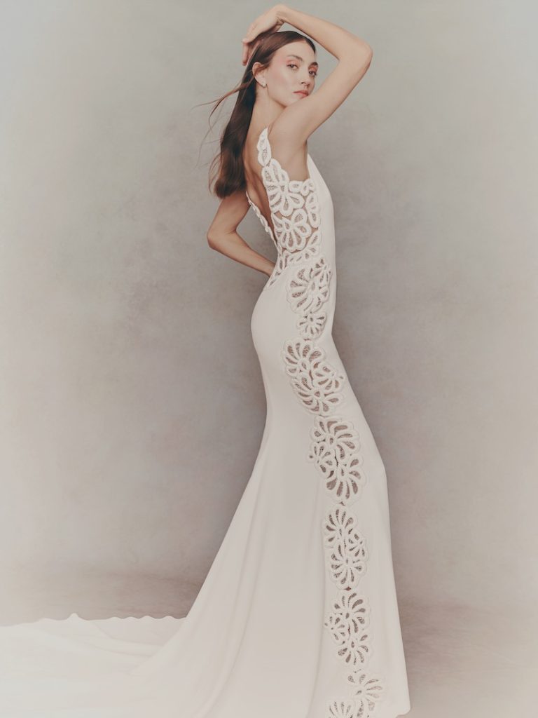 In questa foto una modella posa indossando un abito da sposa a semi sirena in cady con ricami floreali sui fianchi