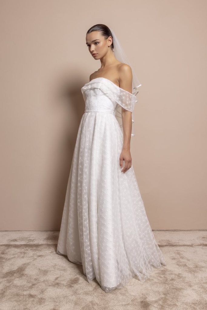 In questa foto, una modella indossa un abito da sposa di Daniela De Souza in tulle plumetis con scollo off shoulder