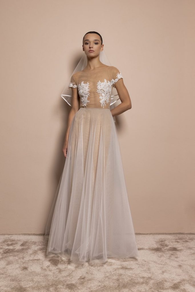 In questa foto, una modella indossa un abito da sposa 2026 in tulle, con ricami effetto tattoo sul corpetto. La modella indossa anche un velo corto con bordo in raso