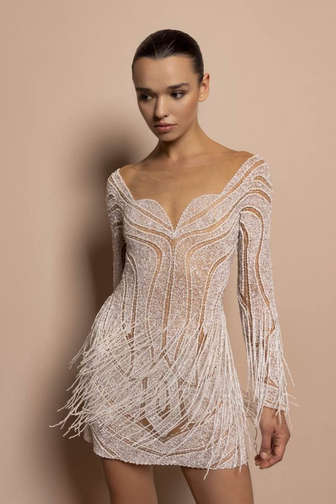 In questa foto, una modella indossa un abito da sposa Daniela de Souza 2026 con motivi geometrici, ricami di perline e paillettes, frange e maniche lunghe