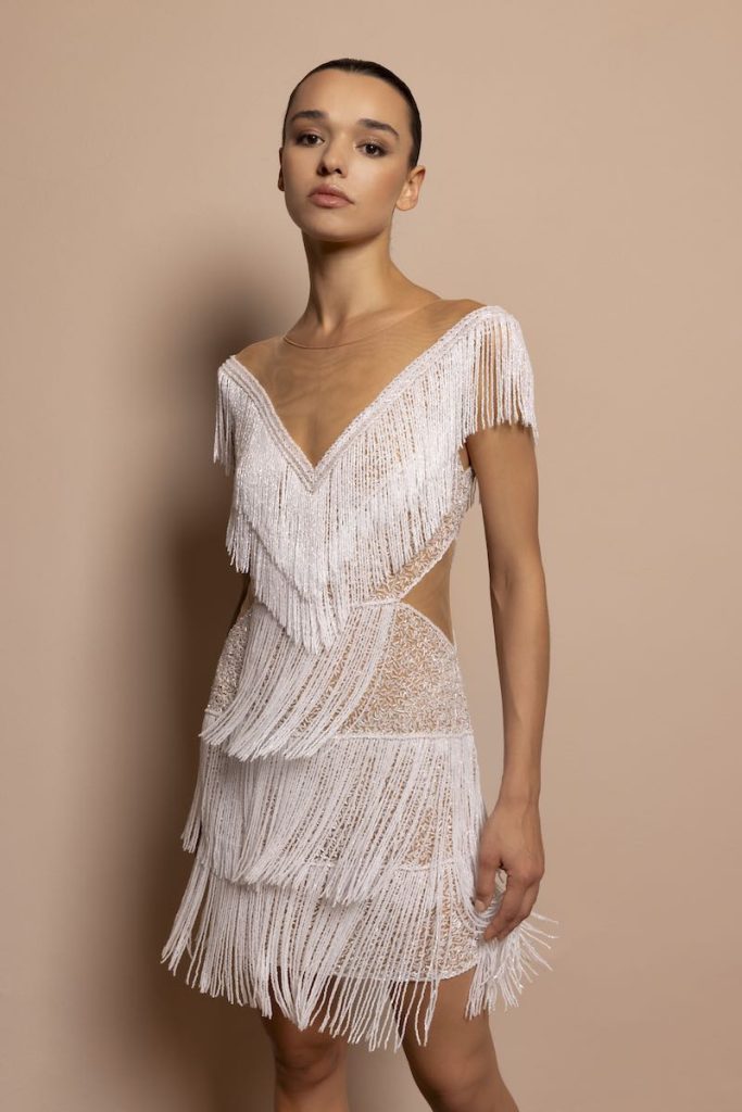 In questa foto, una modella indossa un abito da sposa 2026 di Daniela De Souza con frange di perline, dettagli cut out laterali e scollo a V