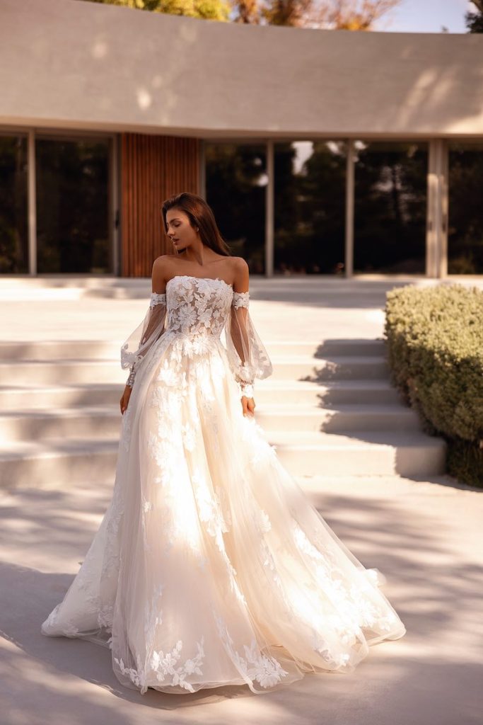 In questa foto, una modella posa indossando un abito da sposa dalla linea ad A in tulle, con ricami floreali sul corpetto e sulle lunghezza e con maniche balloon staccabili