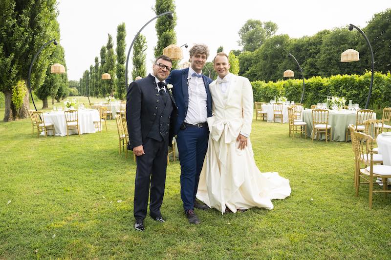 In questa foto, il Wedding Planner Michele Squeri tra i due sposi Alberto e Aldis che posano su un prato davanti all'allestimento del ricevimento di nozze