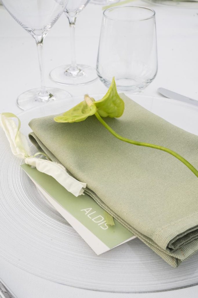 In questa foto, il dettaglio della mise en place del matrimonio di Alberto e Aldis progettato da OttoQuattro Eventi nei toni del verde con tovagliolo, segnaposto, menù e un anthurium di colore verde