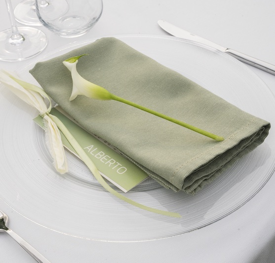 In questa foto, il dettaglio della mise en place del matrimonio di Alberto e Aldis progettato da OttoQuattro Eventi nei toni del verde con tovagliolo, segnaposto, menù e una calla di colore bianco